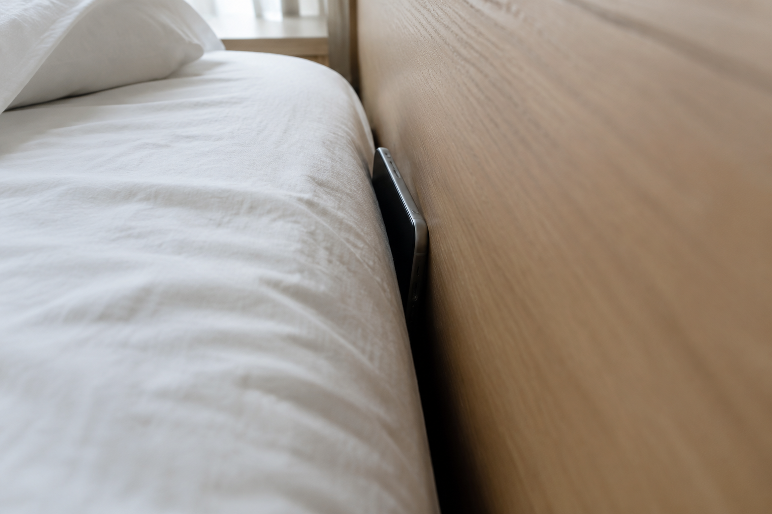 The problem a bed gap filler solves: a phone half swallowed by the gap between mattress and headboard