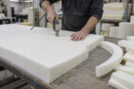 Inside the cushion workshop - a craftsman cutting a circle out of thick upholstery foam with an electric knife along a chalked line