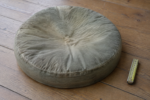 A worn thin old universal round cushion flattened in the center, faded and creased, next to a tape measure - the before picture