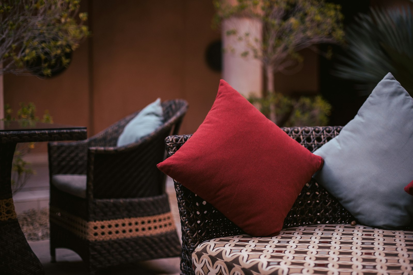 A wicker deep seating group - a club chair and sofa with thick flat-seam seat and back cushions in red and slate fabrics on a covered patio