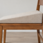 Side profile of a custom wedge seat cushion with a tailored linen cover, ramping from a thin front edge to a taller back edge, resting on a wooden chair seat