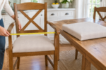 Measuring between the armrests of a dining armchair with a tape measure for replacement cushion sizing